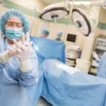 Mature female surgeon in operating suite adjusting latex gloves