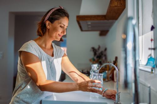 A woman filling up a glass with water at a sink