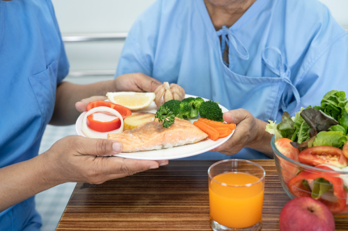 A nurse handing a plate with fruits, vegetables, and fish on it to a patient