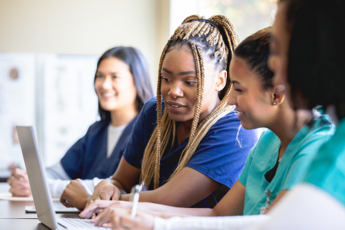 A group of nursing students in a classroom looking at a laptop