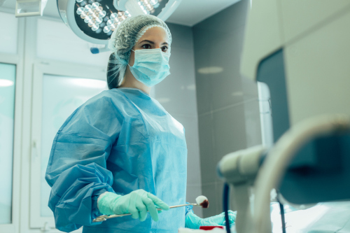 A surgical nurse in an operating room handing forceps to a surgeon