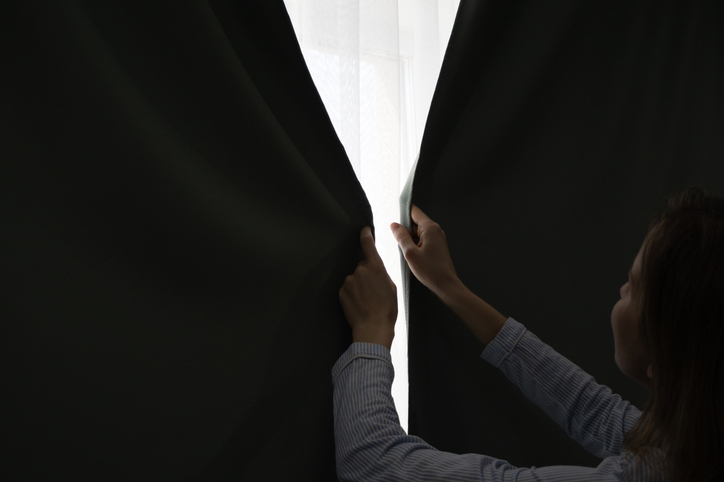 A woman closing blackout curtains in a bedroom